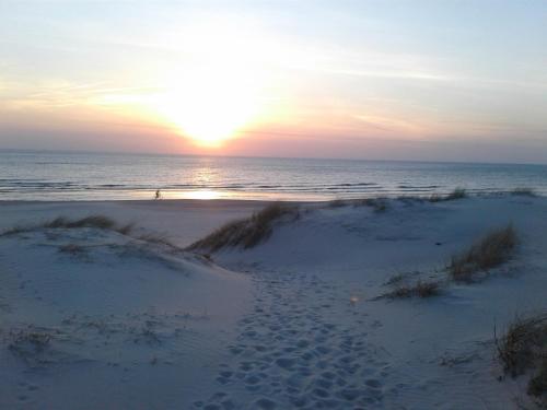 a sunset on a beach with footprints in the sand at Apartamentai su terasa Elija in Šventoji