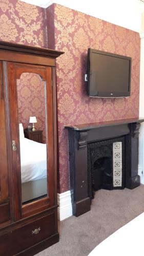 a bedroom with a tv and a bed and a mirror at Branstone Guest House in Llandudno