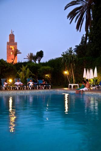 a swimming pool with people sitting on chairs next to a building at Chems Hotel in Marrakech