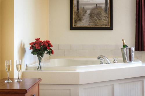 a bathroom with a white tub with a vase of red flowers at Bayside Resort Hotel in West Yarmouth