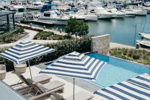 two umbrellas and chairs next to a pool with boats at Anchorage Port Stephens in Nelson Bay