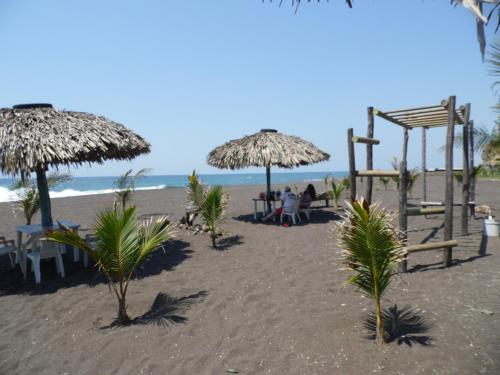 a beach with tables and straw umbrellas and the ocean at Marbella Eco Lodge in Monterrico