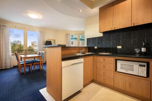 a kitchen with wooden cabinets and a dining room with a table at Quest Savoy in Hobart
