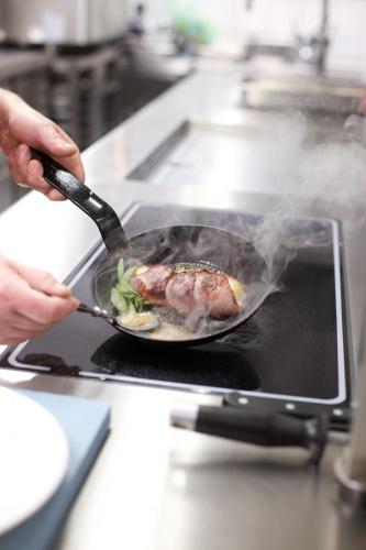 a person cooking food in a pan on a stove at Hotel Reussischer Hof in Schmölln
