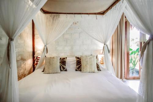 a bedroom with a white canopy bed with curtains at La Cabane in Jimbaran