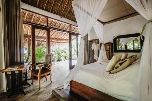 a bedroom with a canopy bed with a desk and a chair at La Cabane in Jimbaran