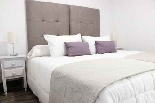 1 dormitorio con 1 cama blanca grande con almohadas moradas en Hostal Castillo, en San José de La Rinconada