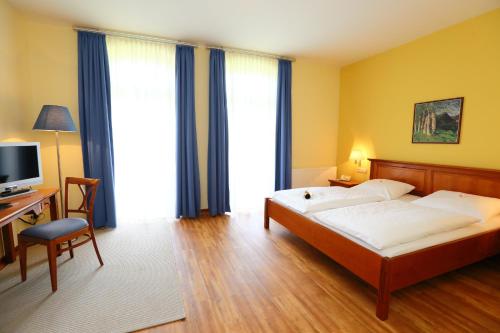 Schlafzimmer mit einem Bett, einem Schreibtisch und einem TV in der Unterkunft Stade Land Golf Hotel in Deinste