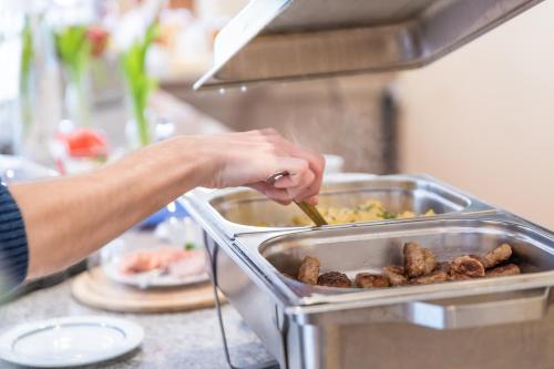 a person stirring a tray of food with a spoon at Hotel Mukran in Sassnitz