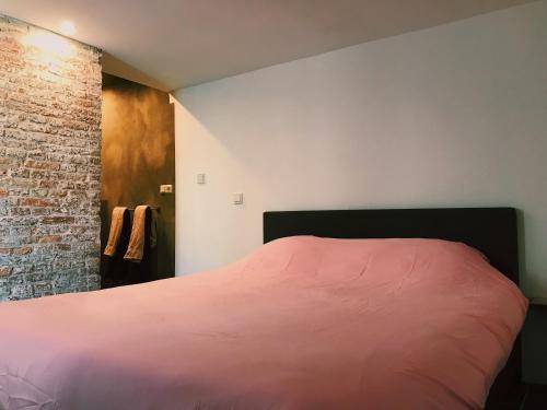 een slaapkamer met een roze bed en een bakstenen muur bij De Pastorie in Middelburg