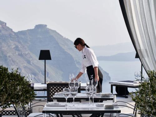 a woman standing over a table with wine glasses at San Antonio - Small Luxury Hotels of the World in Imerovigli