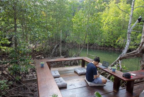 a man sitting at a table with a laptop on a wooden deck at Escape Life Koh Kood in Ko Kood
