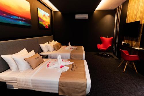 a hotel room with two beds and a red chair at Artworks Hotel Ipoh in Ipoh