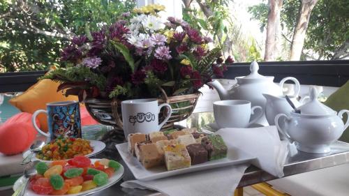 a table with a plate of desserts and cups and flowers at Pearl Holiday Villa in Katunayake