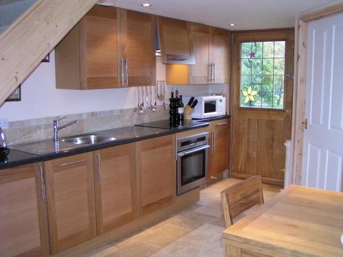 a kitchen with wooden cabinets and a sink and a microwave at Cuddy's Croft in Chatton