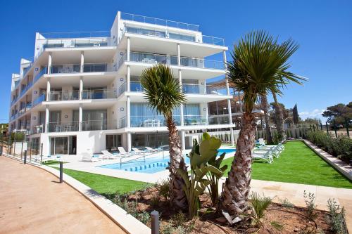 a large white building with a swimming pool and palm trees at Apartaments Posidonia in Colonia Sant Jordi