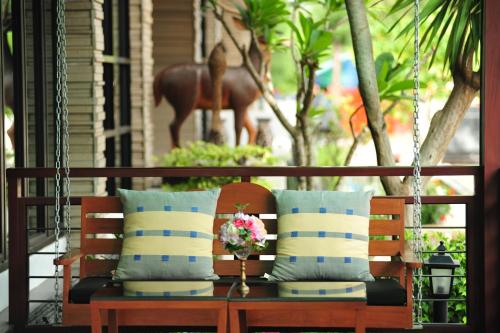 - une balançoire avec des oreillers et un vase de fleurs sur la terrasse couverte dans l'établissement Navarat Heritage Hotel, à Kamphaeng Phet