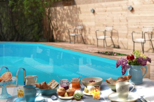 a table with breakfast food next to a swimming pool at Maison du figuier in Lancié