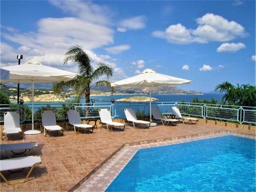 a swimming pool with chairs and umbrellas next to the ocean at Emerald in Plaka