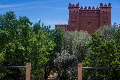 un bâtiment en briques rouges avec une tour au sommet des arbres dans l'établissement Kasbah Ait Kassi, à Boumalne