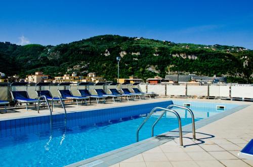 uma piscina com cadeiras azuis e uma montanha em Grand Hotel Cesare Augusto em Sorrento