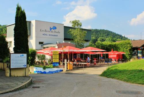 a restaurant with red umbrellas in front of a building at Hotel Les Rives Du Doubs in Les Brenets