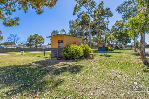 a small yellow house in a park with trees at Boomerang Way Tourist Park in Tocumwal