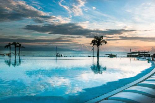 a swimming pool with palm trees and the ocean at AMAZING BEACH FRONT - ACQUA NUEVO VALLARTA - MX in Nuevo Vallarta