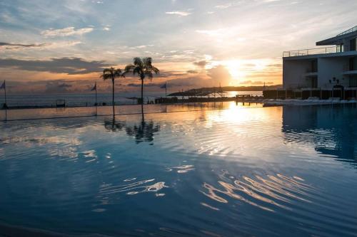 a swimming pool with palm trees and the ocean at sunset at AMAZING BEACH FRONT - ACQUA NUEVO VALLARTA - MX in Nuevo Vallarta