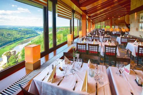 ein Restaurant mit weißen Tischen und Stühlen und großen Fenstern in der Unterkunft Berghotel Bastei in Lohmen
