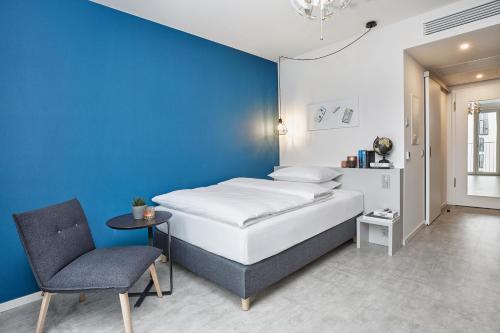 1 dormitorio con una pared azul, 1 cama y 1 silla en H.ome Serviced Apartments München, en Múnich