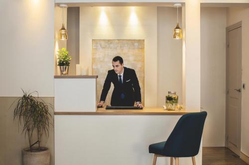 a man in a suit sitting at a counter with a laptop at Hotel Opéra Marigny in Paris
