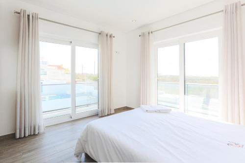a bedroom with a white bed and large windows at Vitamin Sea, The Sea View Apartment in Baleal