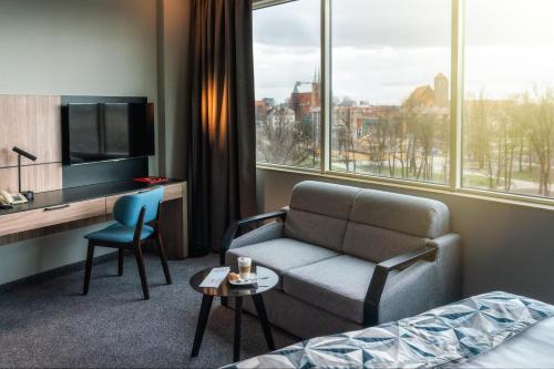ヴロツワフにある HP パーク プラザのソファ、ベッド、テレビが備わるホテルルームです。