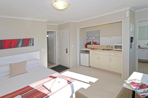 a white bedroom with a bed and a kitchen at Airport Harbour Motel in Auckland