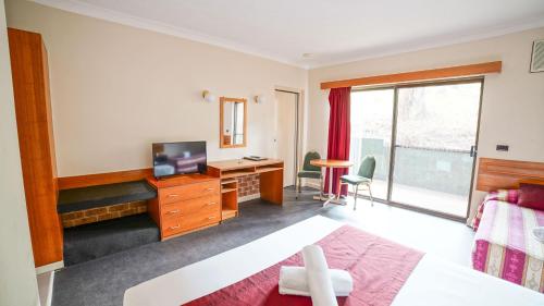 a hotel room with a bedroom with a desk and a television at Country 2 Coast Motor Inn Coffs Harbour in Coffs Harbour