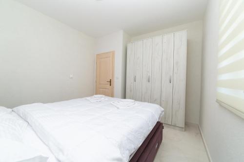 a white bedroom with a bed and a cabinet at Apartmani Tripović in Tivat