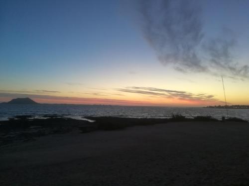 una puesta de sol sobre el océano con una montaña en el fondo en Hormiga's, en Corralejo