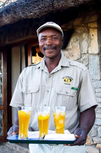 a man holding a tray of glasses of orange juice at Big Cave Camp in Matopos