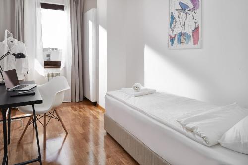 a white bedroom with a bed and a desk with a laptop at Moodeight Apartments in Skopje