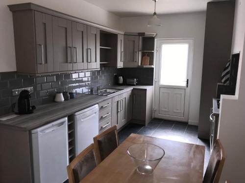 a kitchen with white cabinets and a wooden table at Glens of Antrim Beach House - On the Coast in Glenariff