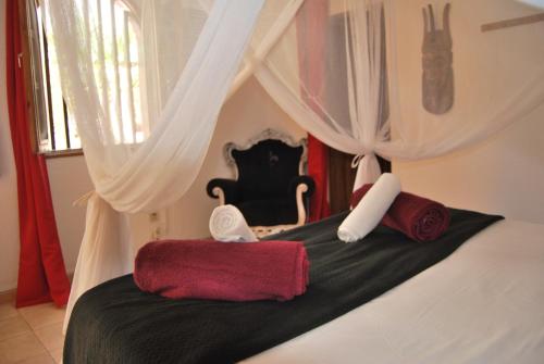 Una cama con cortinas blancas y toallas rojas. en Riad côté jardin, en Saly Portudal
