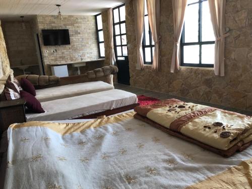a room with two beds and a television and windows at Zimer Al-Bayt in Mas'ade