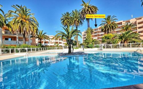 ein großer Swimmingpool mit Palmen vor einem Gebäude in der Unterkunft Appartement T2 de standing au pied des plages in Golfe-Juan