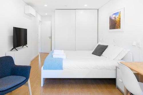 a white bedroom with a bed and a blue chair at East River - T4 junto ao Altice Forum - Braga in Braga
