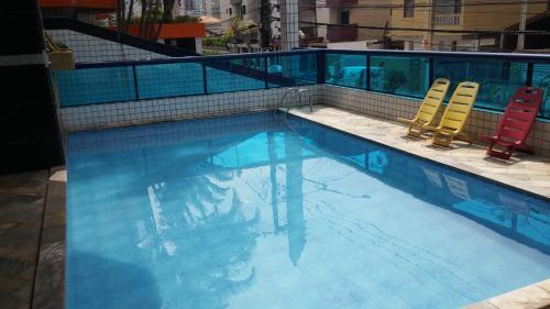 two chairs and a swimming pool with blue water at Apto PROX PRAIA 2 VAGAS GARAGEM, CHURRASQUEIRA SACADA, 3 DORM-GUILHERMINA in Praia Grande