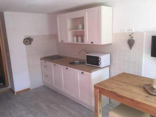 cocina con armarios blancos, fregadero y mesa en Appartamento Dalma Foresta, en Lavarone