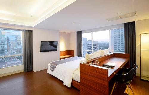 a hotel room with a bed and a desk and window at CROWN PRINCE Hotel Surabaya Managed by Midtown Indonesia in Surabaya