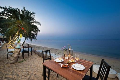 a wooden table with plates of food on the beach at villa Siam View Samui in Ban Bang Po