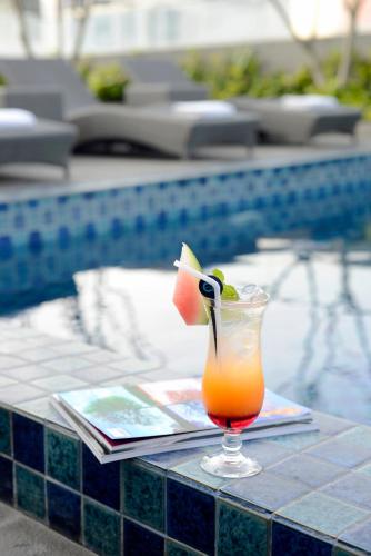 a drink sitting on a table next to a pool at CROWN PRINCE Hotel Surabaya Managed by Midtown Indonesia in Surabaya